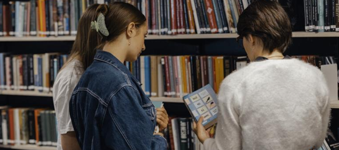 et par personr som ser på en bok på et bibliotek et par personr som ser på en bok på et bibliotek